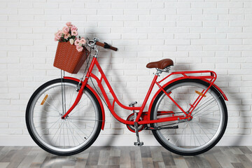 Bicycle with basket of beautiful flowers near white brick wall indoors