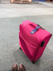 Pink carry-on suitcase at airport gate with visible shoes in frame. Travel preparation, mobility, and passenger experience in transit environment