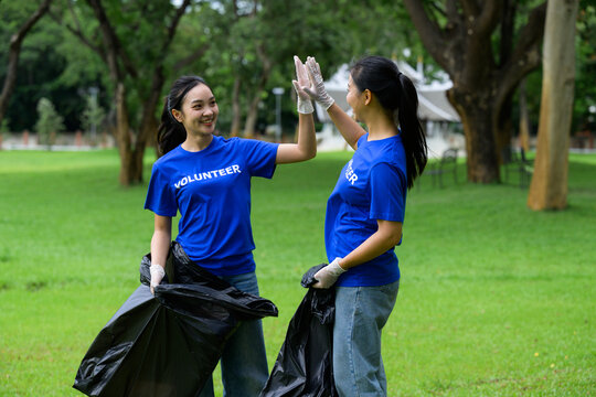 Volunteers giving high five while collecting garbage in park