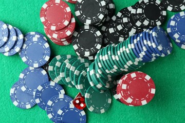 Casino chips and die on green table, flat lay