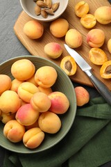 Fresh ripe apricots in bowl, kernels and knife on black table, flat lay