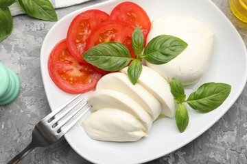 Tasty mozzarella cheese, tomato and basil on grey table, top view