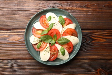 Tasty salad Caprese with mozzarella, tomatoes, basil and spices on wooden table, top view