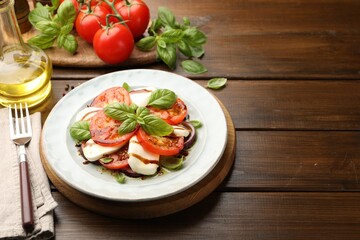 Tasty salad Caprese with mozzarella, tomatoes, basil and spices on wooden table, closeup. Space for text