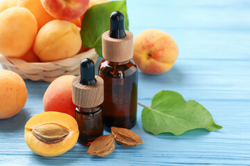 Bottles of essential oil, fresh apricots and kernels on light blue wooden table, closeup. Space for...