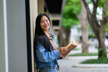 Young student reading a book while leaning against a wall