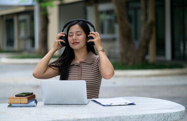 Young woman enjoying music with headphones while working on her laptop outdoors