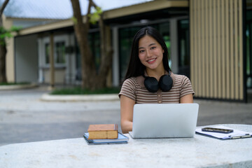 Young asian student studying with laptop and headphones outdoors