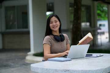Young student working on laptop and reading book outdoors