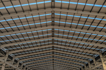 Interior view of an industrial warehouse roof structure with steel beams and skylights, showcasing symmetry, engineering, and modern architectural design