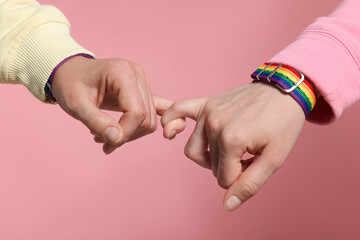 LGBT concept. Women in rainbow wristbands holding hands on pink background, closeup