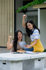Excited students celebrating success looking at tablet sitting at table outdoors