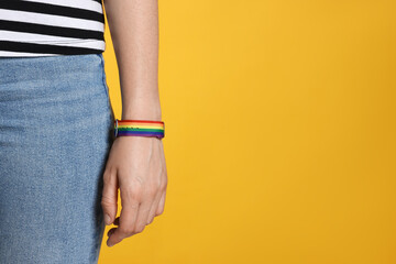 LGBT concept. Woman in rainbow wristband on yellow background, closeup. Space for text