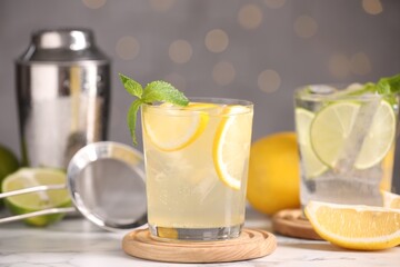 Tasty citrus cocktails in glasses on white marble table against blurred lights, closeup