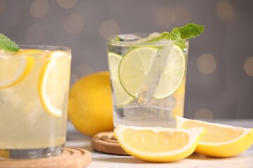 Tasty citrus cocktails in glasses on white table against blurred lights, closeup