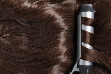 Curling iron with shiny brown hair, top view