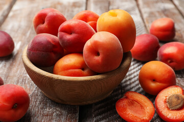 Fresh ripe apricots in bowl on wooden table, closeup