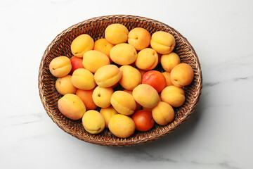 Fresh ripe apricots in wicker basket on white marble table, top view