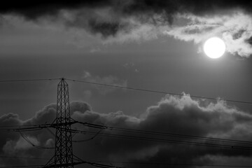 Silhouetted power lines and pylon against dramatic sky in black and white