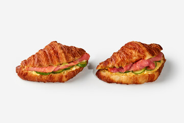 Two delicious croissant sandwiches with salmon, cucumber and cheese filling on white background