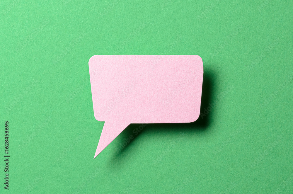 Poster pink cut out paper speech bubble with shadow and copy space for text on green background, close-up f
