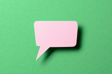Pink cut out paper speech bubble with shadow and copy space for text on green background, close-up...