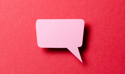 Pink cut out paper speech bubble with shadow and copy space for text on red background, close-up...