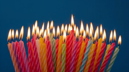 Numerous lit birthday candles in various colors against a blue background colorful
