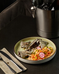 Salmon tartare with avocado, radish, and crispy nori chips on a table with cutlery and ice bucket