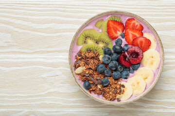 Vibrant and nutritious acai bowl topped with sliced kiwi, strawberries, blueberries, cherries, banana, and granola, a colorful and healthy meal or breakfast on a rustic wooden table, copy space