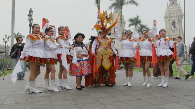 Traditional peruvian dancers and a masked figure pose for photos in front of the municipal palace in plaza mayor, lima