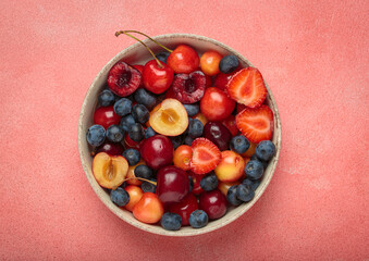 Simple, healthy, and delicious mix of fresh summer fruits is presented in a bowl, sitting on a textured pink background top view