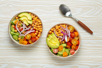 Two bowls of healthy chickpea salad with ripe avocado, juicy cherry tomatoes, crisp cucumber, and...