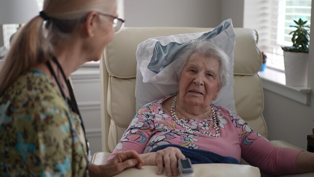 A smiling nurse checks the oxygen levels of an elderly woman using an oximeter during a routine health assessment in a senior living facility.