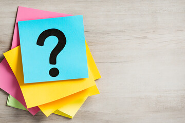 Question mark on colorful sticky notes stack, sitting on a light-colored wood table. Representing uncertainty, problem-solving, brainstorming, or education concepts.