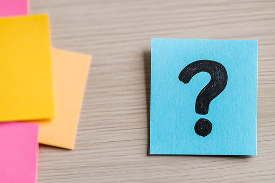 Sticky notes with a question mark on a wooden desk symbolizing uncertainty, inquiry, or brainstorming, surrounded by colorful blank notes.