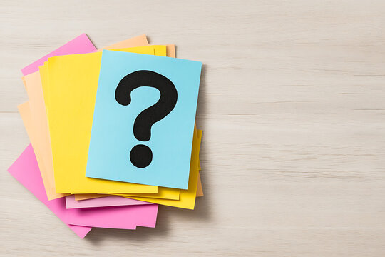 Stack of colorful sticky notes with a question mark printed on a blue one, on a wooden surface. A concept of inquiry and ideas.