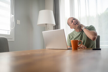 Man suffering from neck pain while working on laptop at home office due to poor posture and...