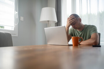 Depressed man sitting at laptop in home office, struggling with life dissatisfaction and sense of...