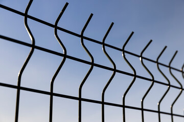 a thin metal lattice fence against a blue sky background, a small thin fence dividing the territory against a sky, closeup