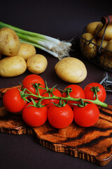 Fresh tomatoes, potatoes and green onions near vegetable peeler on dark background