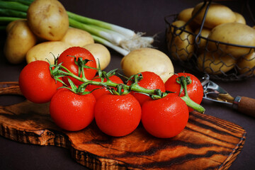 Fresh tomatoes, potatoes and green onions near vegetable peeler on dark background