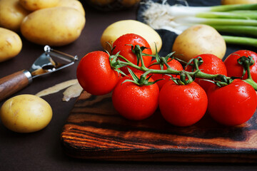 Fresh tomatoes, potatoes and green onions near vegetable peeler on dark background