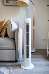 White tower fan against the background of a sofa with colorful pillows in a modern light interior