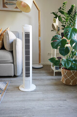 White tower fan against background of flowers and sofa in modern light interior