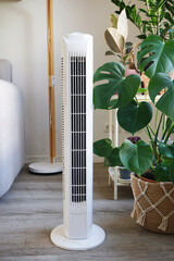 White tower fan against background of flowers and sofa in modern light interior