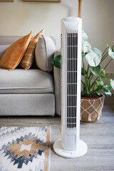 White tower fan against background of flowers and sofa in modern light interior