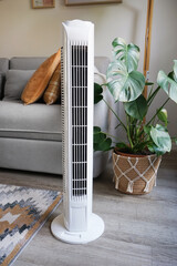 White tower fan against background of flowers and sofa in modern light interior
