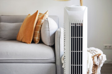 White tower fan against the background of a sofa and a basket with blankets in a modern light...