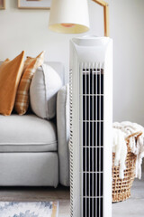 White tower fan against the background of a sofa and a basket with blankets in a modern light...